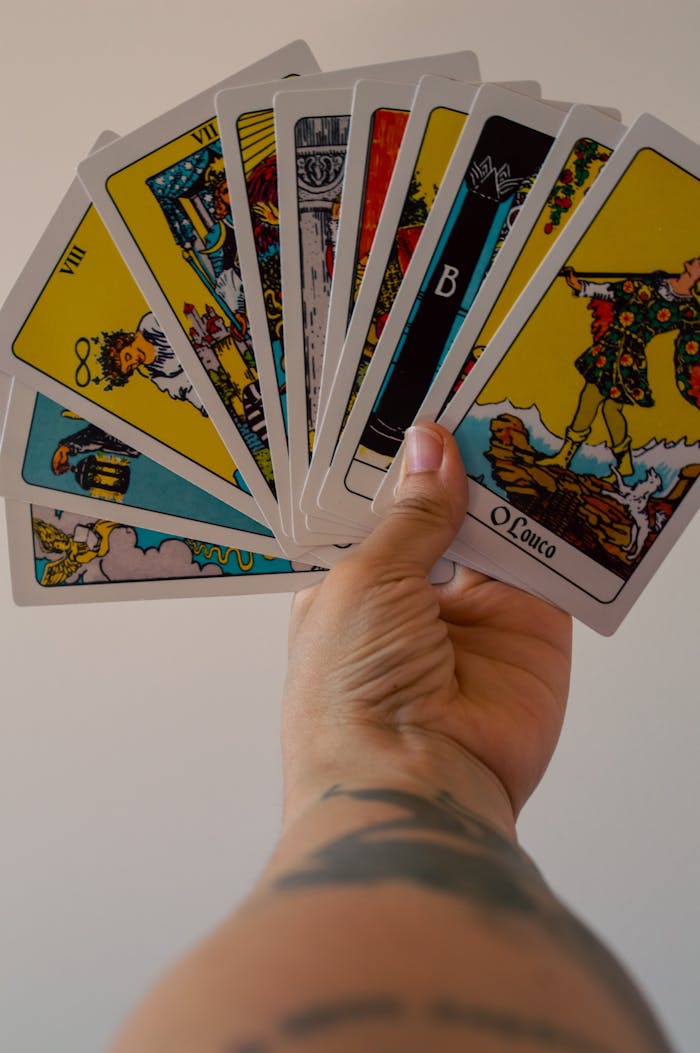 A fan of vibrant tarot cards held in a tattooed hand, displaying unique designs and illustrations.